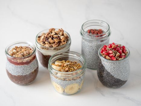 Set of chia pudding in different glass jars on white marble. Assortment of chia puding with different fruits, nuts ingredients. Copy space for text. Superfood,detox,healthy overnight breakfast concept