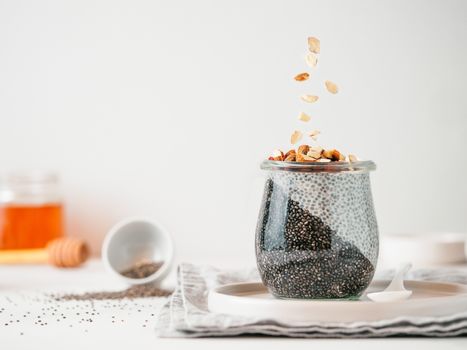 Healthy breakfast concept and idea - two colors chia pudding with organic raw almond. Glass jar with black charcoal and white vegan milk chia pudding with falling chopped almond. Copy space