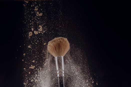 A photograph of Isolated make-up powder with brush on black background