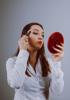Beauty model teenage girl looking in the mirror and applying mascara make up. Beautiful young woman apply makeup
