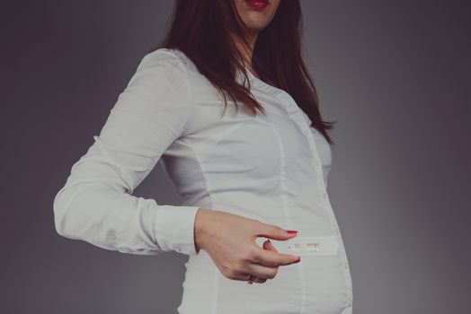 Young woman checking pregnancy test with positive result. Studio shoot.