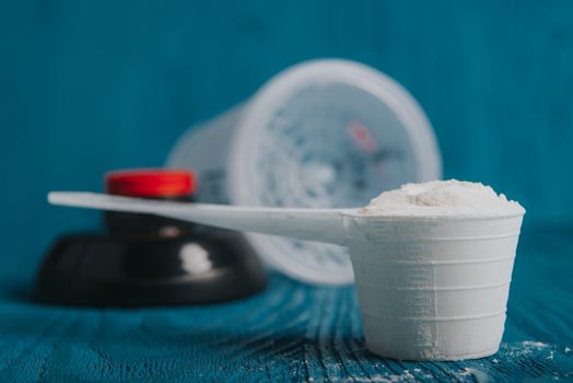 protein supplement powder in plastic spoon on blue wooden background