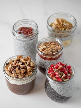 Set of chia pudding in different glass jars on white marble. Assortment of chia puding with different fruits, nuts ingredients. Copy space for text. Superfood,detox,healthy overnight breakfast concept