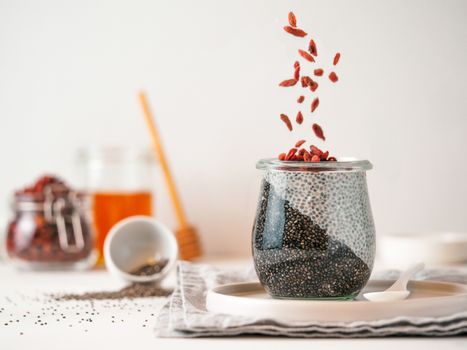 Healthy breakfast concept and idea - two colors chia pudding with organic raw goji berries. Glass jar with black charcoal and white vegan milk chia pudding with falling goji berries. Copy space