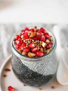 Healthy breakfast concept and idea - two colors chia pudding with organic raw pomegranate, almond and hemp grains. Glass jar with black charcoal and white vegan milk chia pudding. Copy space. Vertical