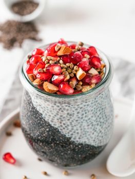 Healthy breakfast concept and idea - two colors chia pudding with organic raw pomegranate, almond and hemp grains. Glass jar with black charcoal and white vegan milk chia pudding. Copy space. Vertical