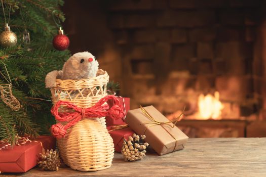 Christmas composition - mouse is symbol of 2020 according to Chinese horoscope in wicker boot under Christmas tree in room by fireplace.