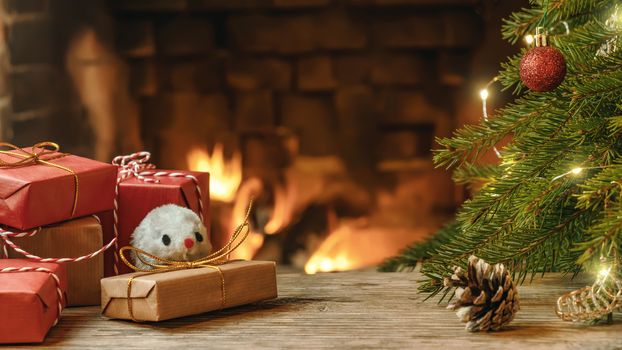 Christmas composition - mouse is symbol of 2020 according to Chinese horoscope next to gifts under Christmas tree in room by fireplace.