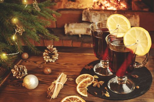 Christmas composition - two glasses with mulled wine on a wooden table near a Christmas tree opposite a burning fireplace.