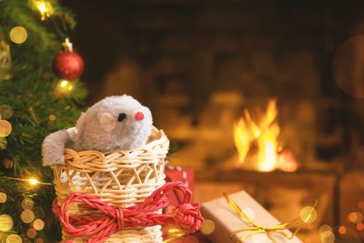 Christmas composition - mouse is symbol of 2020 according to Chinese horoscope in wicker boot under Christmas tree in room by fireplace.