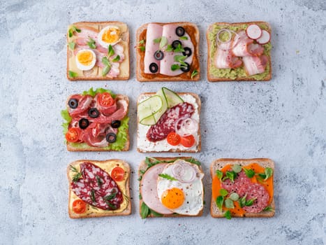 Set of eight different sandwiches with meat in square shape, copy space for text. Top view or flat lay. Assortment meat toasts on gray cement background. Idea, creative concept for sausage maker