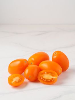Orange tomatoes on white marble table. Yellow or orange tomatoes heap with two half sliced tomato. Copy space for text