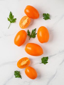 Orange tomatoes on white marble table. Yellow or orange tomatoes with two half sliced tomato and fresh parsley leaves. Top view or flat lay. Vertical composition.