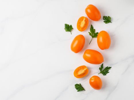 Orange tomatoes on white marble table. Yellow or orange tomatoes with two half sliced tomato and fresh parsley leaves. Copy space for text. Top view or flat lay.