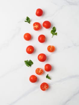 Orange tomatoes on white marble table. Small red cherry tomatoes with half sliced tomato and fresh parsley leaves. Top view or flat lay. Vertical composition. Copy space for text.