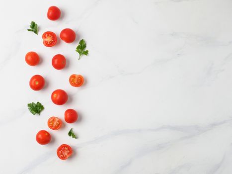 Orange tomatoes on white marble table. Small red cherry tomatoes with half sliced tomato and fresh parsley leaves. Top view or flat lay. Copy space for text.