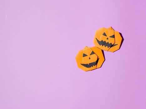 Halloween concept. Paper origami pumpkin on bright purple background. Simple idea for halloween - easy made paper pumpkins on trendy Crocus Petal lilac color background. Copy space for text.