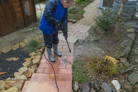 Woman cleans stone slabs with a pressure washer