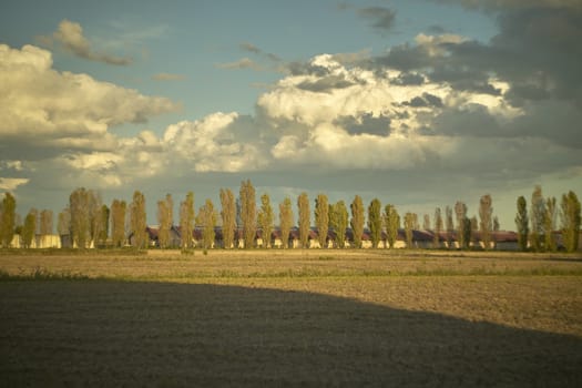 Country landscape resold at ground level, where you can see the remains of a newly threshed culture, the sky and the clouds and a typical country house in northern Italy on the bottom.