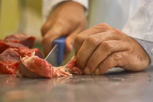 butcher who using a knife is slicing the meat in order to be sold and later eaten in his butcher's shop.