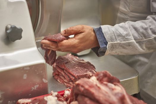 Butcher trying to sliced calf steaks with the udo of the electric slicer in his butcher's shop.