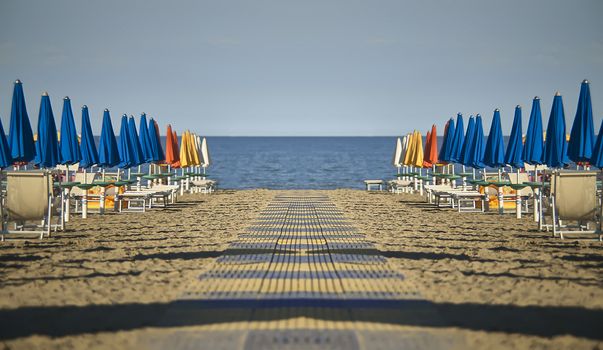 Perfectly specular and symmetrical view of the beach with umbrellas and loungers of Lignano sabbia d'oro in Italy. A scene devoid of people who give emotions of calm and peace as only the sea can do.