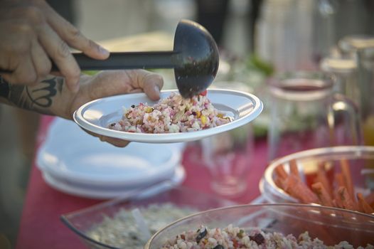 Waiter who is using a ladle with freshly prepared rice salad. Quality italian food. Typical Italian cuisine.