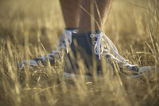 Shoe in the foreground with behind the other while being worn by a boy walking in the grass.