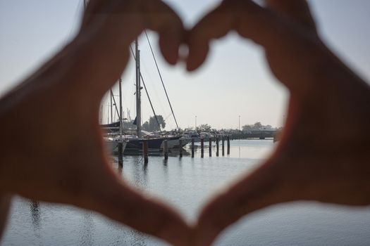 View of a landscape of a seaport with as a frame a heart made with hands.