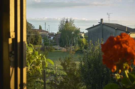 View from the open window of a rural landscape typical of the small villages of the Po Valley in Italy with flowers and plants in full bloom. Villanova del ghebbo, Italy location of the photo.