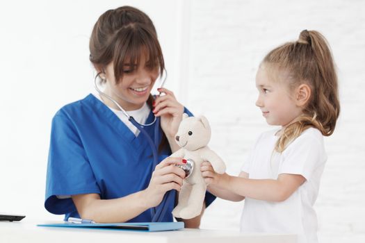 Young smiling female doctor and her little patient with teddy bear