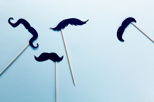 Group of accessories in form of black moustaches on sticks on grey blue background with copy space. Concept men's health, prostate cancer awareness month, charity, Father's Day. Flatlay.