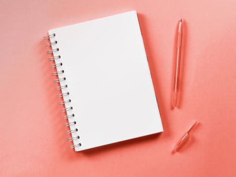 Top view of blank note paper with pen on pliving coral color background. Color of year 2019 Living Coral concept. Top view or flat lay. Copy space for text. Vertical.