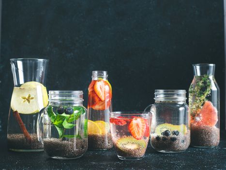Different chia water in glass on dark background. Chia infused detox water with berries, fruits and herbs. Healthy eating, drinks, diet, detox concept. Copy space for text