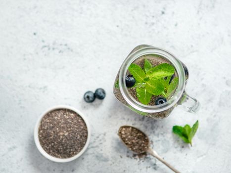 View from above chia water in mason jar with mint and blueberry on gray cement background.Chia infused detox water with berries.Copy space for text.Top view. Healthy eating, drinks, diet,detox concept