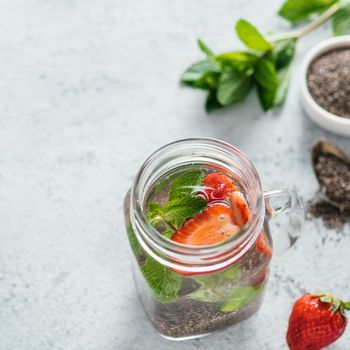 View from above chia water in mason jar with strawberry and mint on gray cement background. Chia infused detox water with berries. Copy space for text. Healthy eating, drinks, diet, detox concept