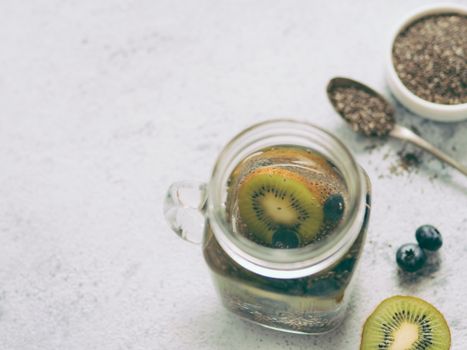 View from above chia water in mason jar with kiwi and blueberry on gray cement background. Chia infused detox water with berries. Copy space for text. Healthy eating, drinks, diet, detox concept