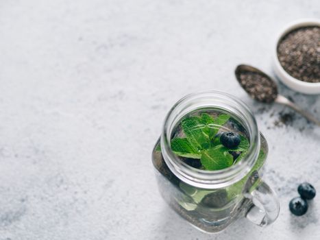 View from above chia water in mason jar with mint and blueberry on gray cement background. Chia infused detox water with berries. Copy space for text. Healthy eating, drinks, diet, detox concept