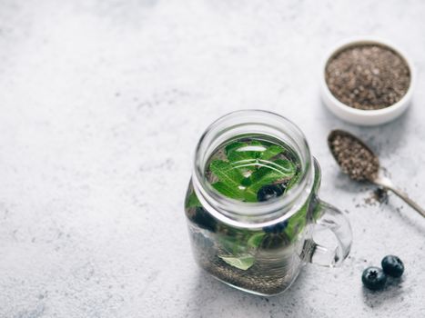 View from above chia water in mason jar with mint and blueberry on gray cement background. Chia infused detox water with berries. Copy space for text. Healthy eating, drinks, diet, detox concept