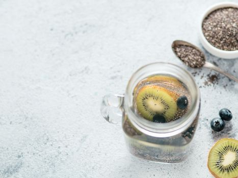 View from above chia water in mason jar with kiwi and blueberry on gray cement background. Chia infused detox water with berries. Copy space for text. Healthy eating, drinks, diet, detox concept