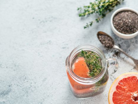 View from above chia water in mason jar with grapefruit and thyme on gray cement background. Chia infused detox water with berries. Copy space for text. Healthy eating, drinks, diet, detox concept