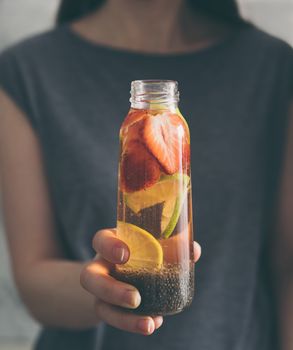 Woman hand with chia water. Glass bottle with chia detox water with lime and strawberry. Toned image. Dark or low key. Selective focus.Healthy eating, drinks, diet, detox, wellbeing and people concept