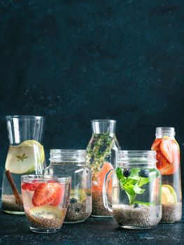 Different chia water in glass on dark background. Chia infused detox water with berries, fruits and herbs. Healthy eating, drinks, diet, detox concept. Copy space for text. Vertical.