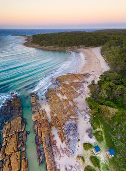 Beach panorama at dusk with soft motion in waves and rocky shoreline exposed in low tide