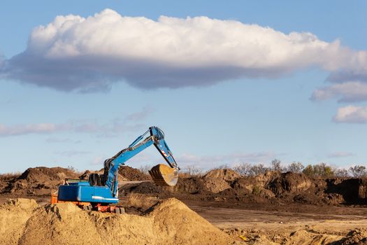 Excavator at sandpit during earthmoving works, in the background the blue sky