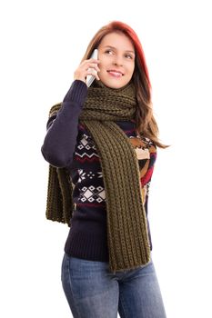 A portrait of a smiling beautiful young girl in winter clothes talking on a phone, isolated on white background.
