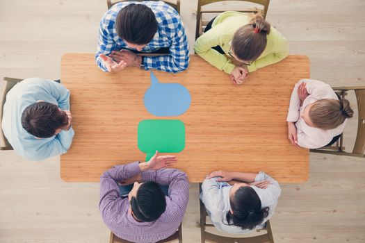 Team of business people in casual clothes sitting around the table with paper dialog boxes, discussing opinion concept