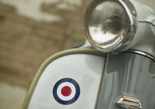 Detail of the front and back of a vintage scooter wet with rain droplets with a very high detail detail. White vointage scooter with areografie.