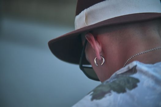 View of the neck and head of a boy with earrings and hat looking down. Symbol of sadness, depression and social discomfort.
