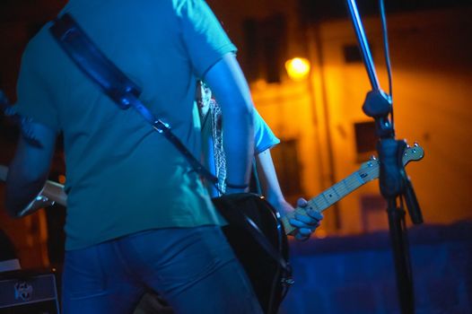 Detail of a rock musician who plays the bass in live at a concert with smoke and soft lights. Artistic photo with the filtered shot of the lights.